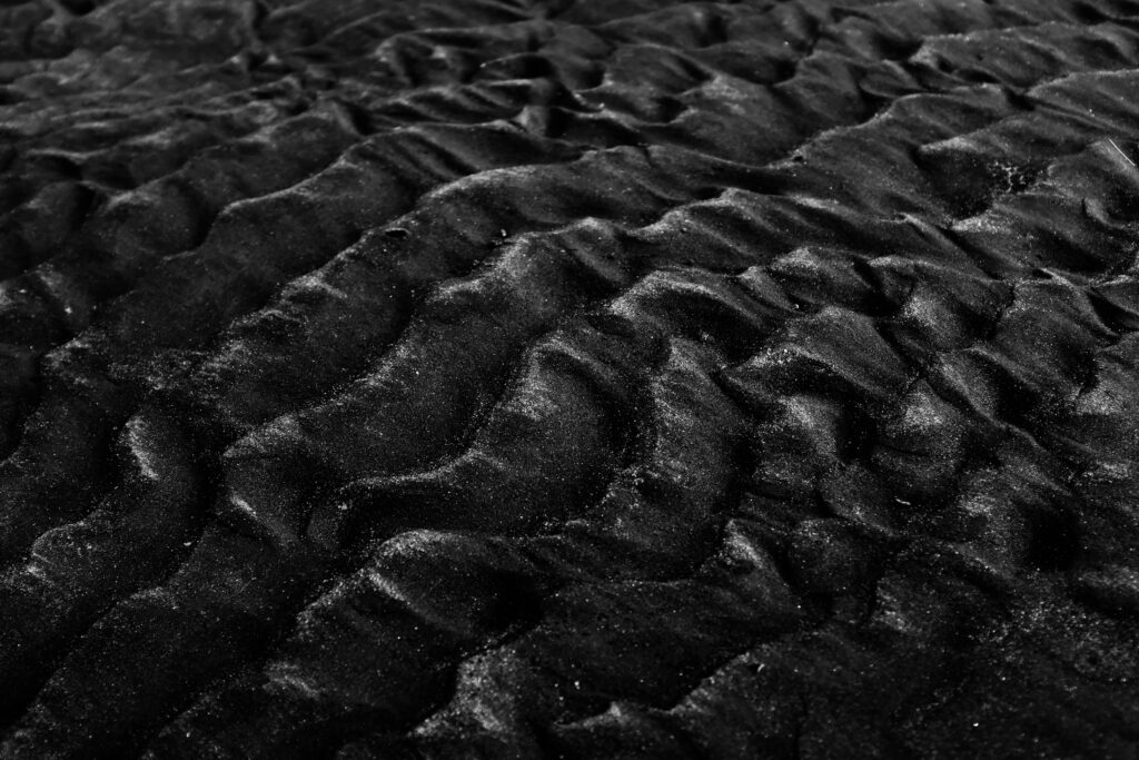 Close-up of textured black sand dunes in monochrome, showcasing natural patterns and textures.